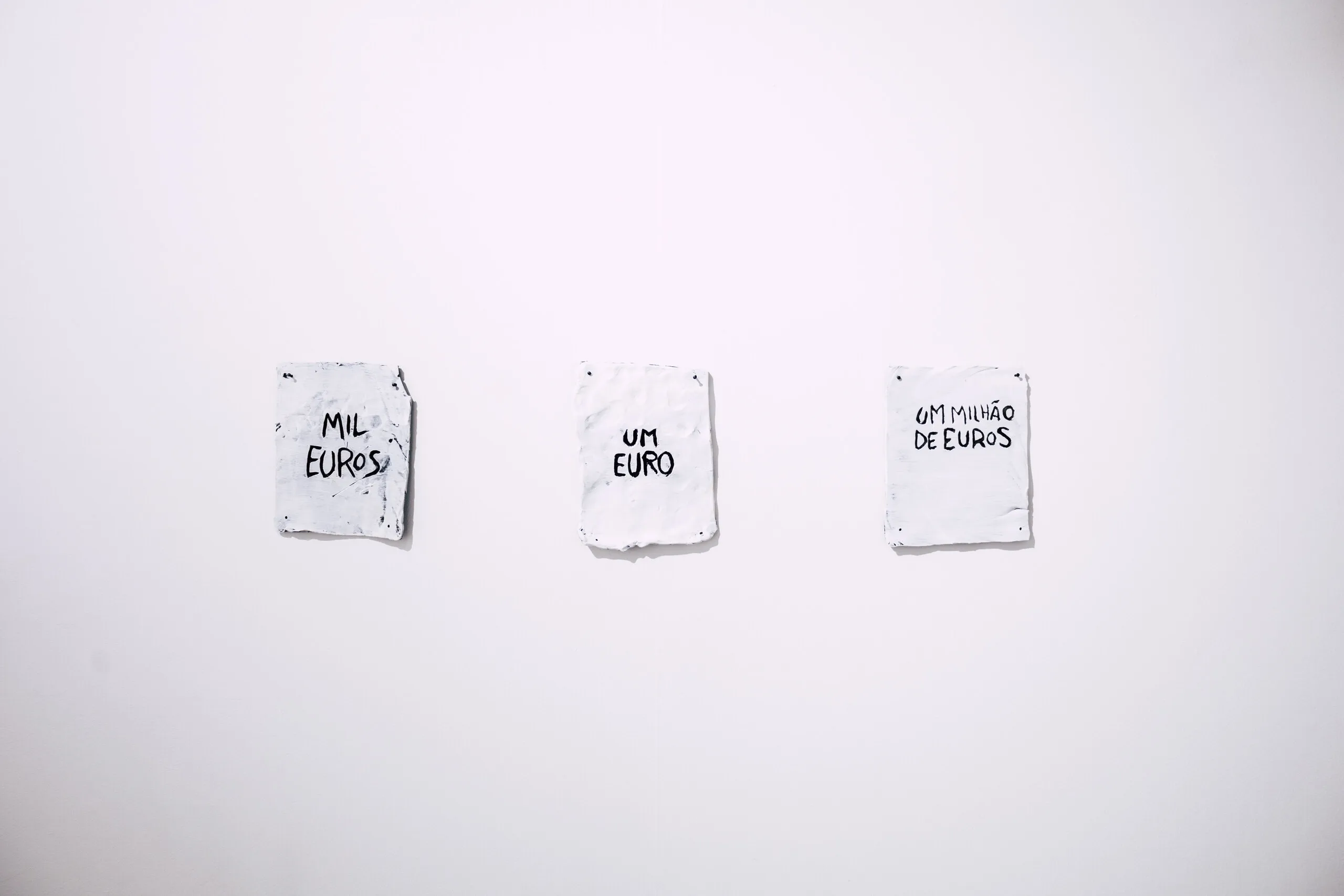 Espelho Meu: three small white pieces with handwritten text, hung in a row. Photo: Jenniffer Lima Pais